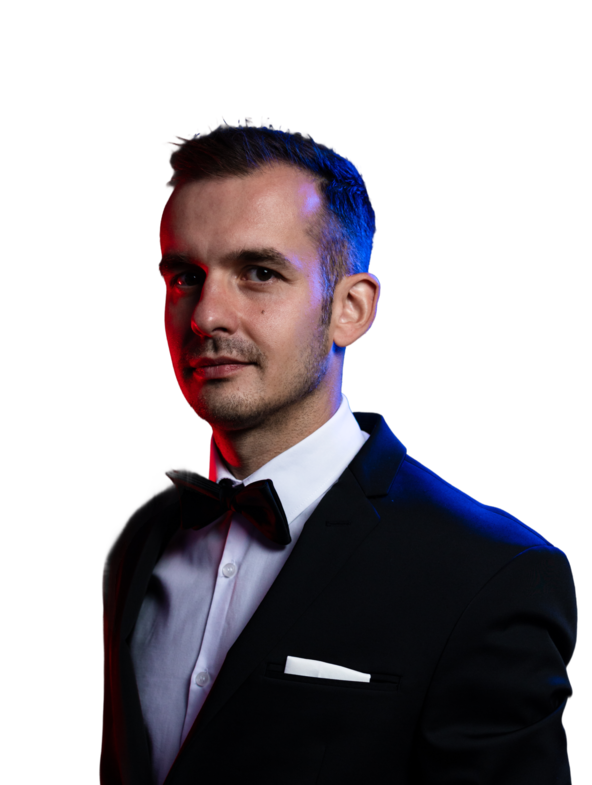 Denys in Anzug mit Fliege, dunklem Hintergrund und blauen Lichtakzenten.